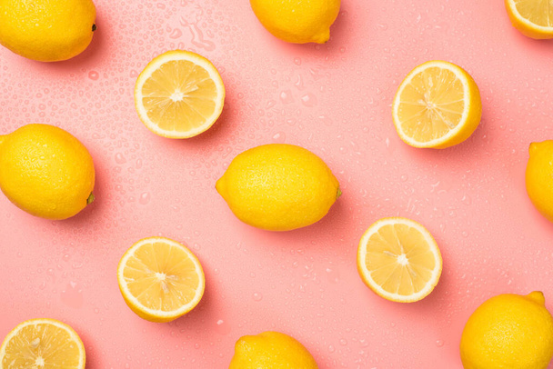 Photo de tête de gouttes d'eau coupées et de citrons jaunes entiers sur fond rose pastel isolé - Photo, image