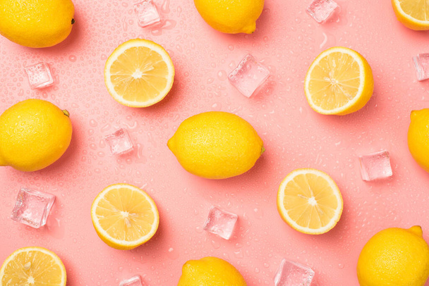 Вид сверху фото кубиков льда капли воды половинки и целые желтые лимоны на изолированном розовом фоне пастели - Фото, изображение