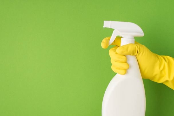 Overhead photo of cleaning spray and hands in yellow gloves isolated on the green background - Photo, Image