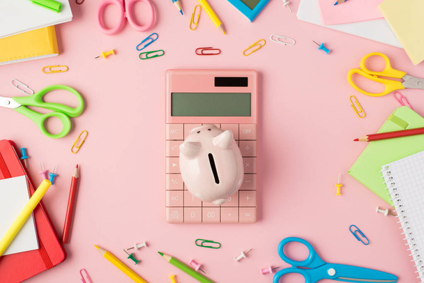 Foto vista superior de papelería multicolor tijeras bolígrafos lápices pinzas clips planificadores y alcancía sobre calculadora rosa aislado pastel fondo rosa - Foto, imagen