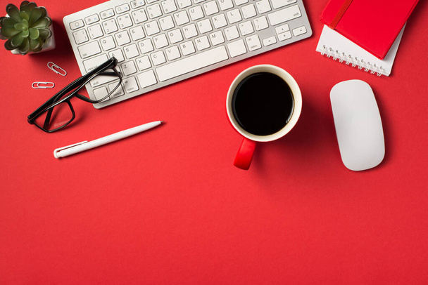 Draufsicht Foto der weißen Tastatur-Maus Blumentopf Gläser Clips Stift rote Tasse Kaffee und zwei Notizbücher auf isolierten lebendigen roten Hintergrund mit Copyspace - Foto, Bild
