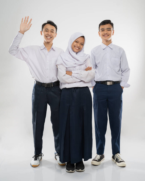 Three teenagers in junior high school uniforms stand smiling at the camera while greeting with a hand gesture - Foto, imagen