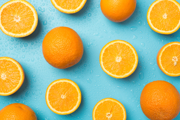 Bovenaanzicht foto van waterdruppels verspreid gesneden en hele sinaasappels op geïsoleerde lichtblauwe achtergrond - Foto, afbeelding