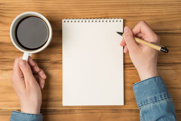 Yleiskuva kannettavan paperin kädet kynällä ja kuppi kahvia eristetty puinen tausta - Valokuva, kuva