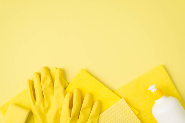 Top view photo of cleaner gel bottle yellow sponge viscose rags and rubber gloves on isolated yellow background with copyspace - Photo, Image