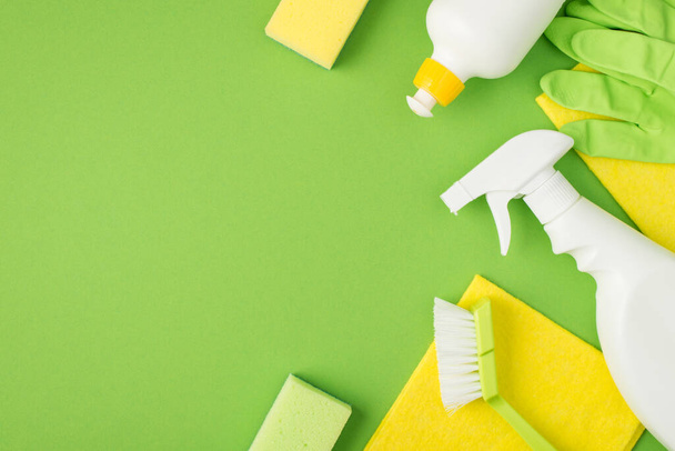 Foto vista superior de detergente spray y gel botellas esponjas cepillo trapos amarillos guantes de goma verde sobre fondo verde aislado con copyspace - Foto, Imagen