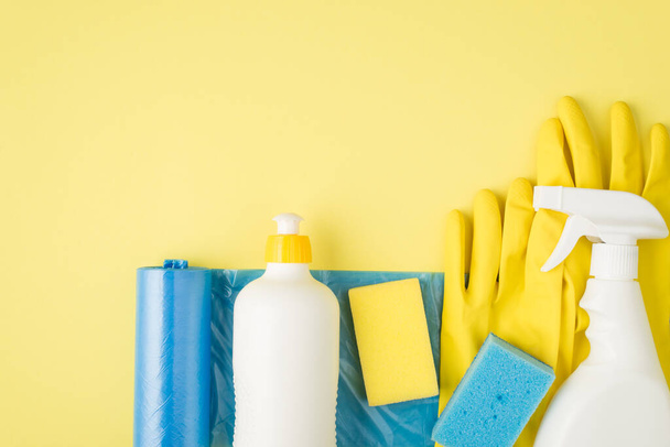 Foto vista superior de bolsas de basura azul spray detergente y botellas de gel esponjas guantes de goma sobre fondo amarillo aislado con espacio en blanco - Foto, imagen