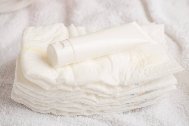 Foto de primer plano del tubo de crema blanca sin etiqueta en pañales sobre fondo textil blanco aislado - Foto, Imagen