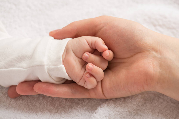Foto de primer plano de la pequeña mano del bebé recién nacido en la palma de la madre sobre un fondo textil blanco aislado - Foto, imagen