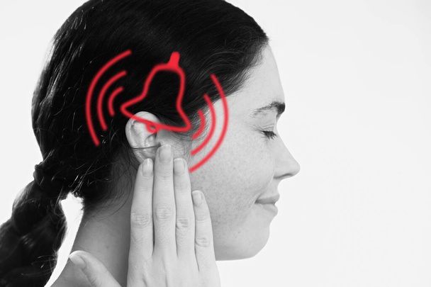 Tinnitus. A dissatisfied young woman holds her hand over her ears, experiencing ringing and pain. The concept of ear diseases and deafness. - Photo, Image