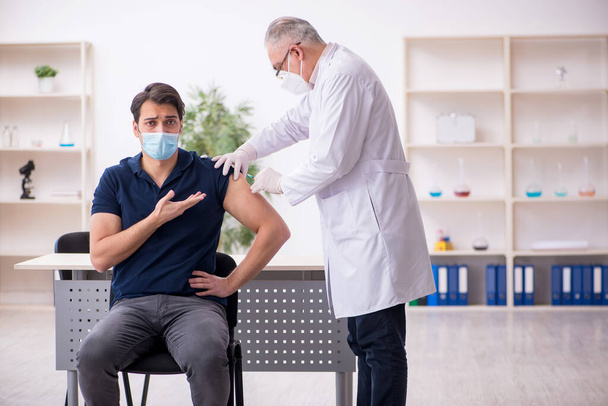 Jeune patient de sexe masculin visitant un vieux médecin en conce de vaccination - Photo, image