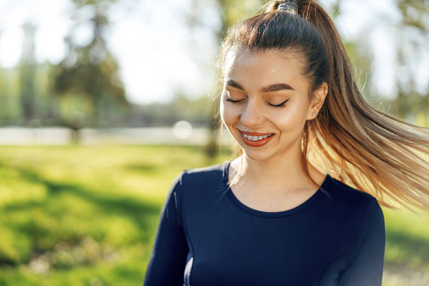 Portrait of a young smiling woman wearing sportswear in morning park - Фото, зображення