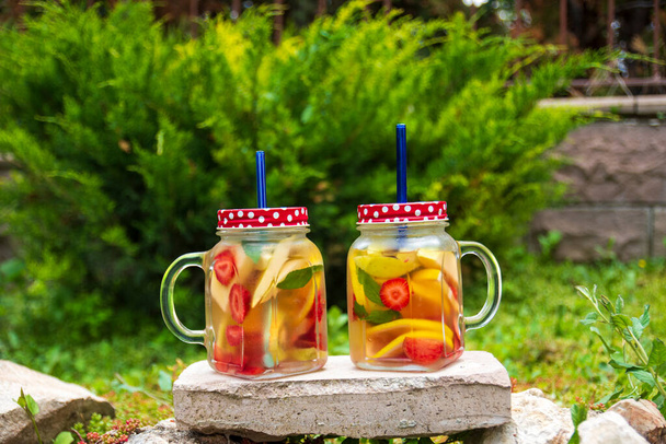 Két üveg üveg, finom méregtelenítő ital piros, narancs és sárga gyümölcsökkel, a kövön áll. Szelektív fókuszáló szemüveg. - Fotó, kép