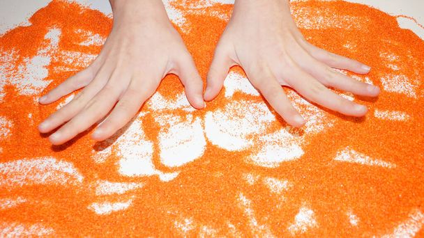 hands of a teenager on orange kinetic sand sand therapy for autism. - Photo, Image