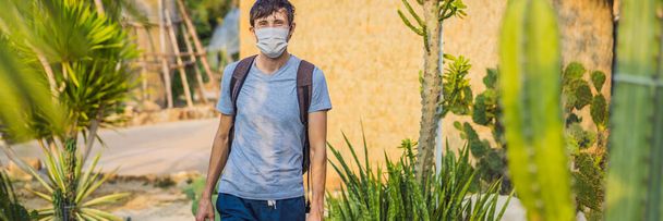 BANNER, LONG FORMAT beautiful stylish young man in desert among the cacti, wearing a medical mask during COVID-19 coronavirus, traveling in Africa on safari, exploring nature, sunny summer, traveler - Foto, imagen
