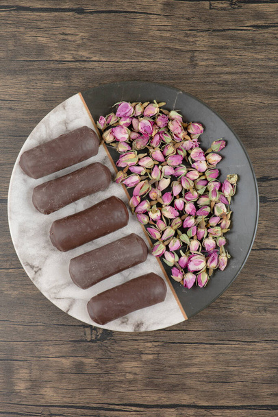 Un plato lleno de rollos de crema de chocolate con crema de leche con rosas secas en una mesa de madera. Foto de alta calidad - Foto, Imagen