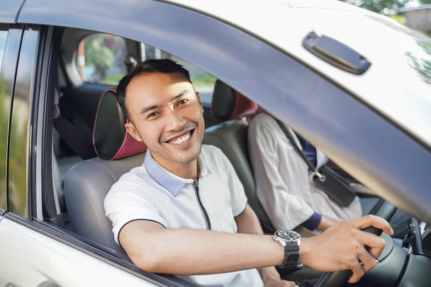 a young asian man laughing looking at the camera while driving in a car - Fotoğraf, Görsel