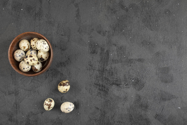 Wooden bowl of organic raw quail eggs on black surface. High quality photo - Foto, afbeelding