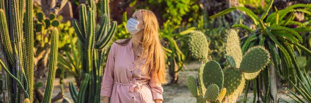 BANNER, LONG FORMAT beautiful stylish young woman in pink dress in desert among the cacti, wearing a medical mask during COVID-19 coronavirus, traveling in Africa on safari, exploring nature, sunny - Foto, Bild