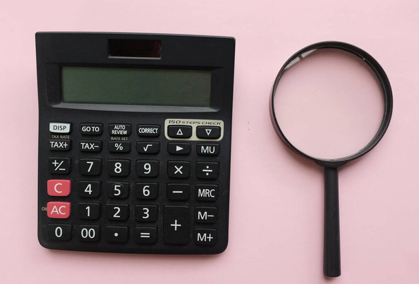 top view és lapos feküdt fekete nagyító üveg és számológép rózsaszín pasztell háttér.Üzleti és pénzügyi koncepció - Fotó, kép