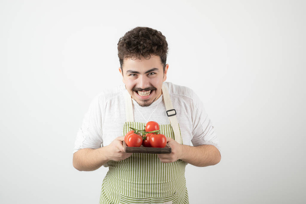 Un gars souriant tenant une pile de tomates sur un plateau avec les mains. Photo de haute qualité - Photo, image