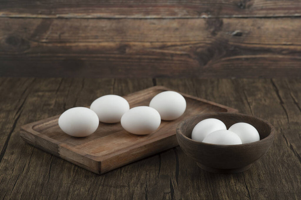 Ξύλινη σανίδα και μπολ γεμάτο βιολογικά ωμά αυγά σε ξύλινο φόντο. Υψηλής ποιότητας φωτογραφία - Φωτογραφία, εικόνα