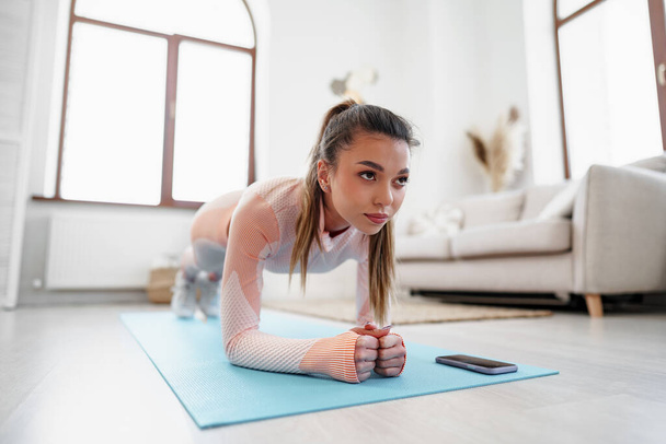 Sporty young woman doing plank exercise indoors at home - Фото, зображення