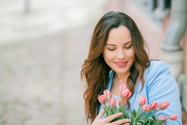 Portrait of a beautiful young woman in a blue suit with a bouquet of tulips. - Photo, Image
