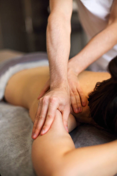 Безликий мастер делает массаж спины и плечевых мышц анонимной женщине, лежащей на столе в спа-салоне - Фото, изображение