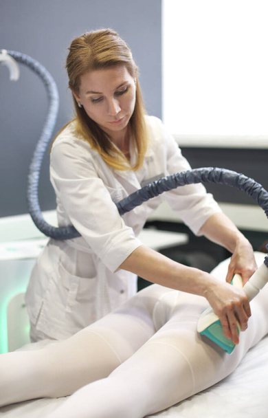 Косметолог, який використовує пристрій для схуднення LPG на тілі жіночого клієнта в білому костюмі, лежить на дивані
 - Фото, зображення