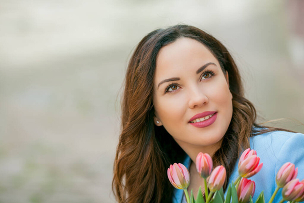 Portrait of a beautiful young woman in a blue suit with a bouquet of tulips. - Photo, Image