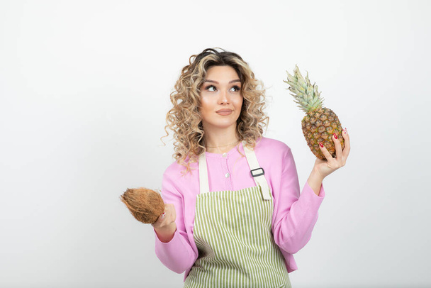 Beautiful curly woman in apron holding tropical fruits over white. High quality photo - Photo, Image
