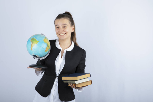 Photo of young teacher holding books and globe on white background. High quality photo - Foto, Imagem