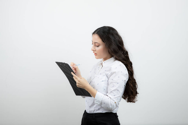Успешная деловая женщина пишет в блокноте карандашом о белую стену. Высокое качество фото - Фото, изображение