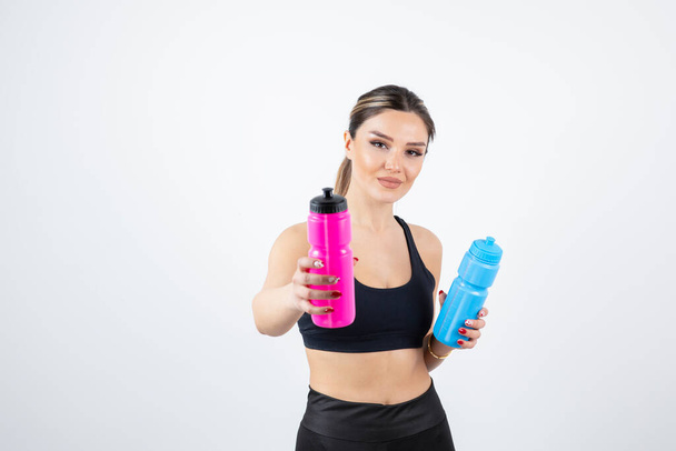 Portrait of young athletic woman holding blue and pink water bottles. High quality photo - Photo, Image