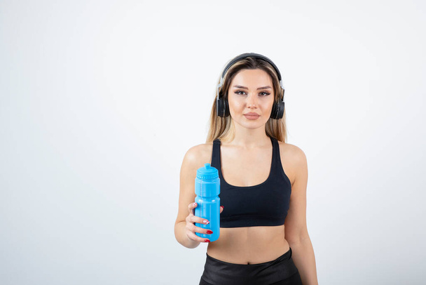 Mulher desportiva bonita em fones de ouvido segurando garrafa com água. Foto de alta qualidade - Foto, Imagem