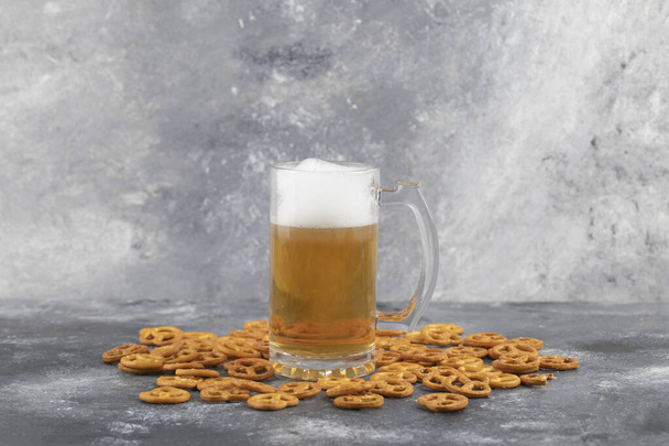 Кружка холодного пенного пива и соленые крендельки на мраморном фоне. Высокое качество фото - Фото, изображение