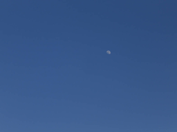 Темно-синє небо, забарвлене далеким віддаленим місяцем вдень. Глибоке блакитне небо з гордістю має білу крапку - місяць - це відображає сонячне світло в приємний весняний вечір
. - Фото, зображення