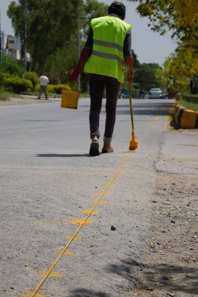 Un giovane operaio che indossa un giubbotto di sicurezza sta dipingendo manualmente cartelli stradali. - Foto, immagini