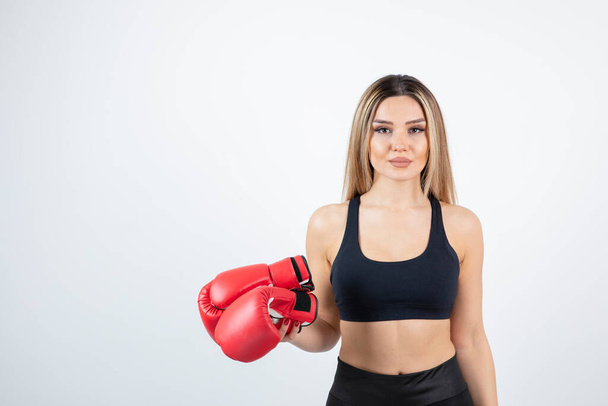 Young blonde woman in crop top holding red boxing gloves. High quality photo - Photo, Image