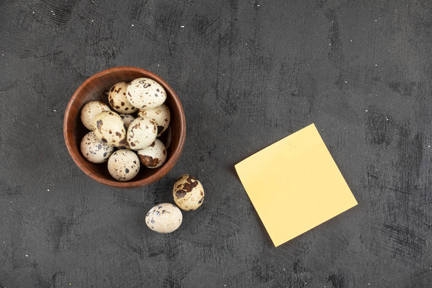 Cuenco de madera de huevos de codorniz crudos orgánicos y papel blanco amarillo en la superficie negra. Foto de alta calidad - Foto, imagen