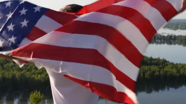Sarışın çocuk nehir kıyısında mavi gökyüzünde ulusal Amerikan bayrağı sallıyor. - Video, Çekim
