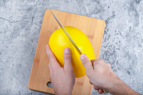 Hands cutting fresh yellow melon on wooden cutting board. High quality photo - Fotó, kép