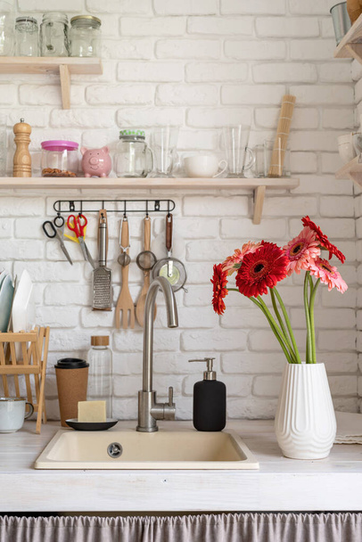 Rustic kitchen interior with white brick wall and white wooden shelves. Fresh gerbera flowers in a white vase - Photo, Image