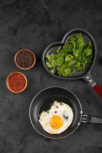 Жареное яйцо на сковороде с зеленью и приправами на черной поверхности. Высокое качество фото - Фото, изображение