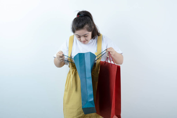 Rozkošná mladá dívka s Downovým syndromem hledající uvnitř nákupních tašek. Kvalitní fotografie - Fotografie, Obrázek