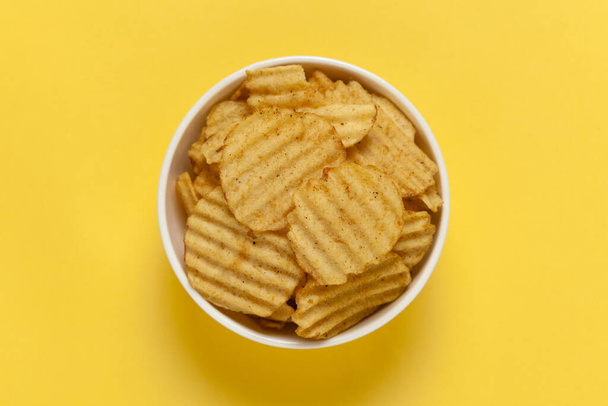 Крупним планом зморшкуваті хвилясті картопляні чіпси в білій керамічній мисці, популярний готовий їсти хрусткий, солоний блідо-жовтий колір на жовтому тлі
 - Фото, зображення