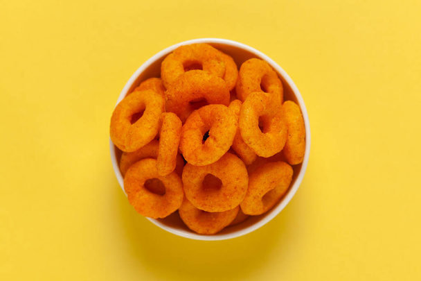 Close up of Popular Készen áll, hogy enni ropogós és puffadt snackek gyűrű cseresznyés narancs színű kerámia tál, sós fehér kerámia tál sárga háttér felett - Fotó, kép