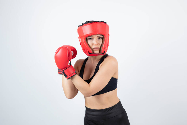 Portret van jonge vrouwelijke bokser in rode handschoenen en helm training. Hoge kwaliteit foto - Foto, afbeelding
