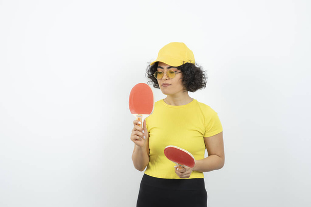 Masa tenisi raketi tutan kıvırcık saçlı genç kızın stüdyo portresi. Yüksek kalite fotoğraf - Fotoğraf, Görsel